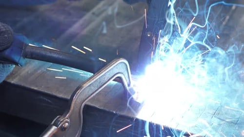 Trabajo de cerca con metal, acero y hierro con una máquina de soldar, chispas y destellos brillantes en cada s.