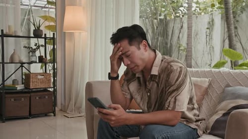 Man on Couch Looks Stressed While Using Phone