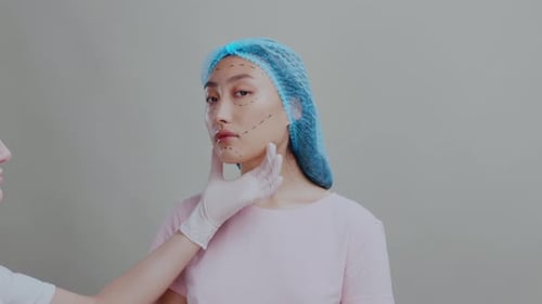 Chinesische Asiatin bereitet sich auf eine plastische Chirurgie vor, bei der die Hände des Kosmetikers das Gesicht berühren
