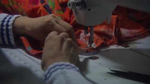Statische Mittelaufnahme einer Person, die mit Stoffen und Textilien an einer Nähmaschine arbeitet