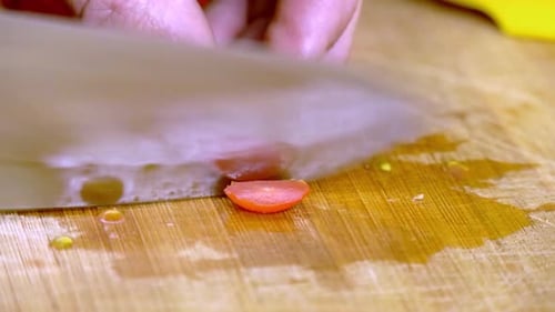 Male cutting a red cherry tomato with a very sharp silver knife on a wooden cutting board. Close up