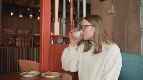 Side View of Student in Glasses Enjoying Latte in Cozy Coffee Shop