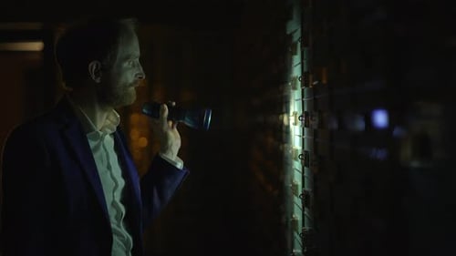 Man Inspects Server Rack with Flashlight at Night