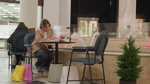 Woman Notes During Retail Pause Female Shopper Relaxed with Coffee and Notes Casual Daytime Shopping