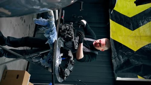 Vertical Video Service Station Auto Mechanic Unscrews the Bolts in the Headlight in Part of the Car