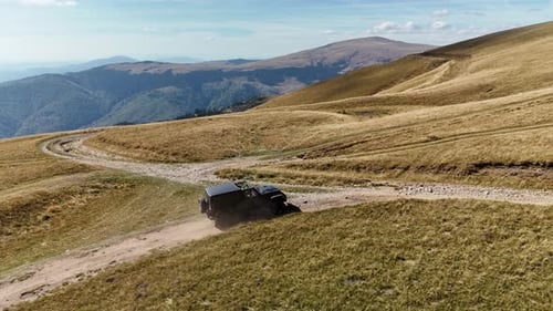 Geländewagen fährt auf kurvigem Feldweg durch hügelige Landschaft