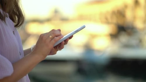 Woman Holding Phone in Sunny Urban Setting