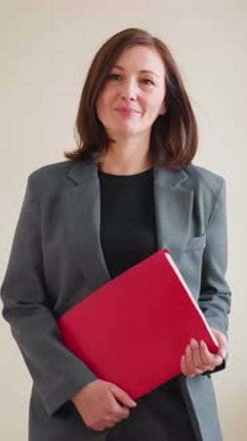 Confident Businesswoman Walking Holding Red Folder in Office Hallway