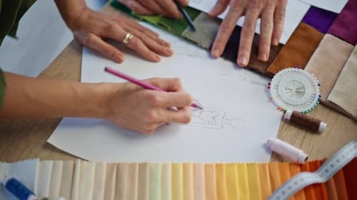 Stylisten beim Zeichnen von Kleidungsskizzen am Schreibtisch des Ateliers, Nahaufnahme von zwei Künstlern