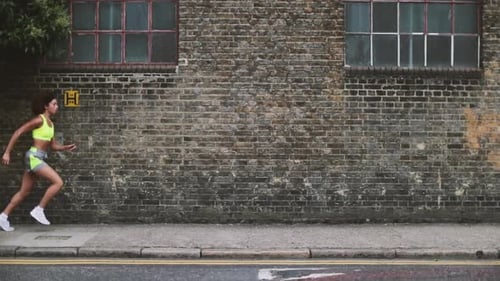 Woman Running Fast Past Brick Wall in Urban Area