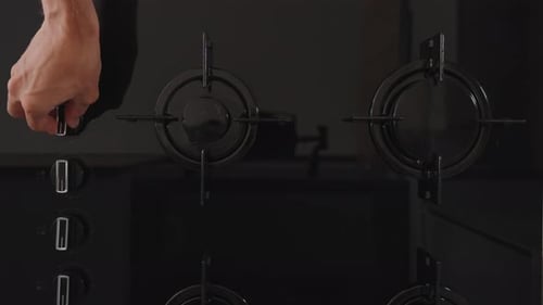 A black glass gas stove with four burners. I turn the knob and ignite one of them. Top-down view.