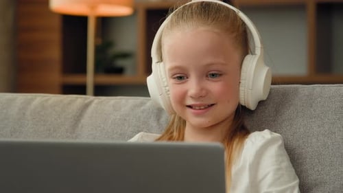 Child Listens to Laptop with Headphones on Couch