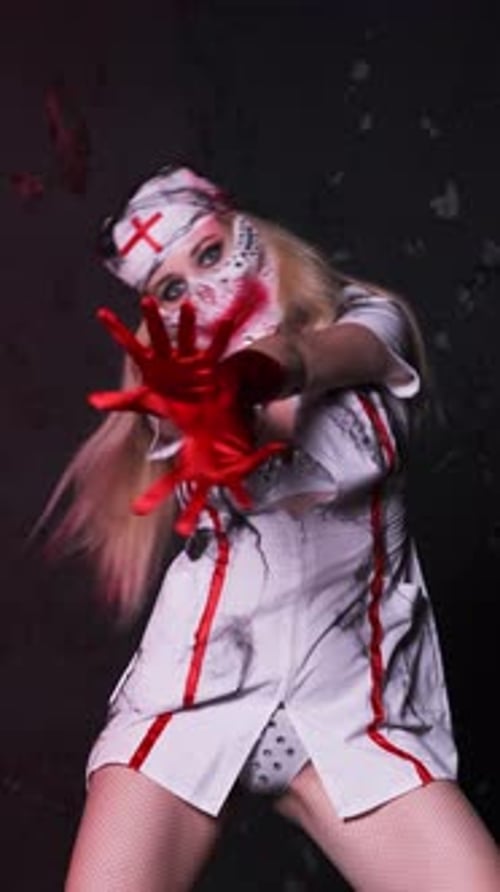 Beautiful sexy girl in scary nurse costume, red gloves and scary mask for Halloween dancing on black