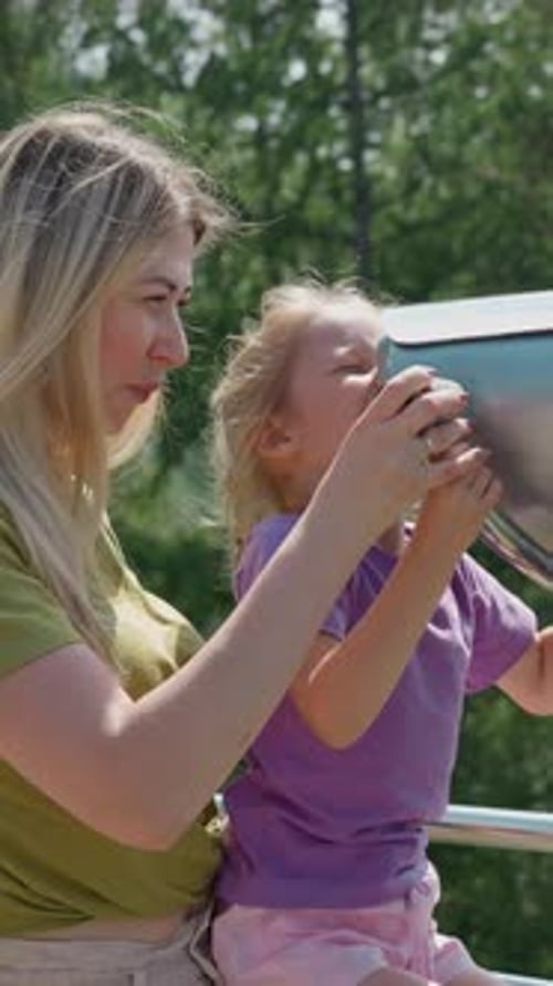 Mother Helps Girl Look Through Binoculars at Resort Deck