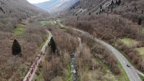 Aerial: passenger train in a valley by a river and a road with light traffic in the Pyrenees, southe