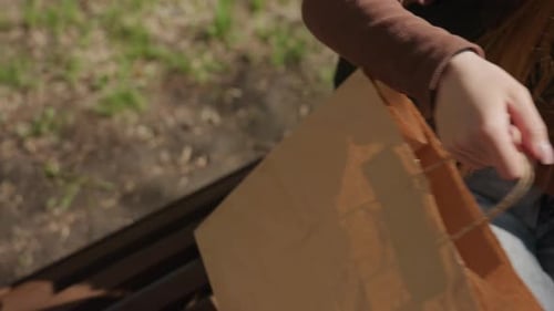 Mujer coloca una bolsa de papel en el banco y luego se aparta, silenciosos listones de madera vacíos enmarcados por la luz del sol y