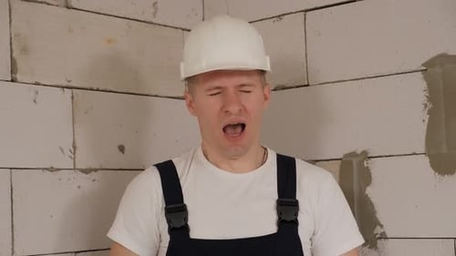 A Tired Construction Worker in a White Hard Hat is Standing in a New Apartment
