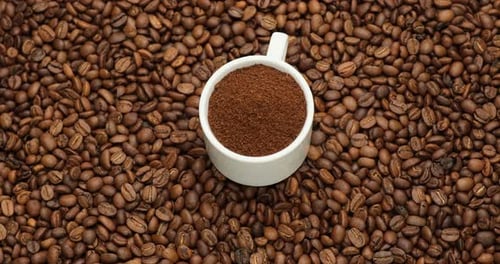 Tasse en céramique pleine de café moulu sur un fond rotatif de grains de café fraîchement torréfiés