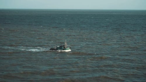 Slow motion shot of a small fishing boat sailing through the Indian ocean while seagulls follow.