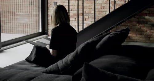 Back view on young woman sitting on comfortable sofa and reading book