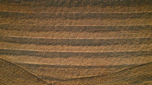 Patterns created on the soil of a freshly plowed field from an aerial perspective resembling waves.