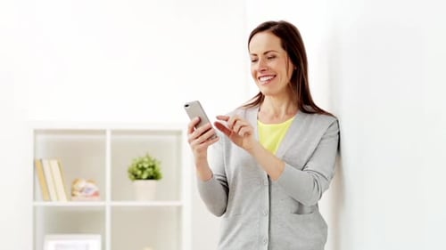 Smiling woman using mobile phone in bright home
