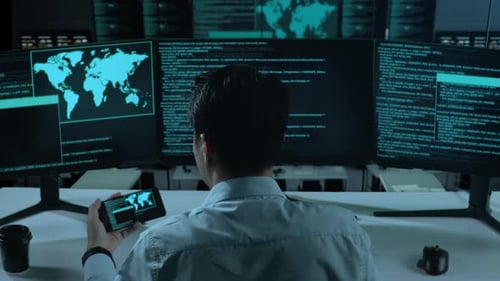 Happy Asian Man Looking At Code On Mobile Phone While Write Code With Multiple Screens In office