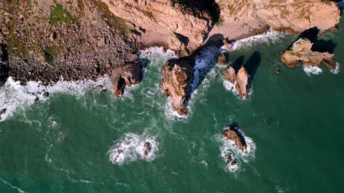 Eine atemberaubende Luftaufnahme der Küstenfelsen und der lebhaften Surfwellen von oben über dem Meer