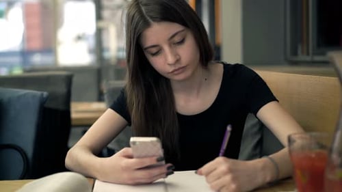 Teenage Girl with Smartphone Doing Homework Sitting in Cafe Alone