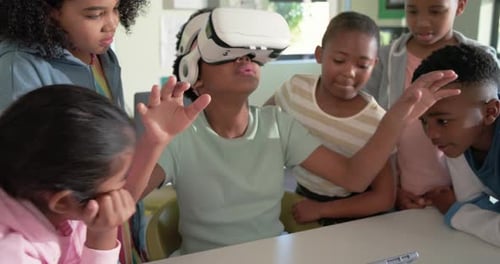 African-American teen girl with VR headset, mint tee, gesturing to VR demo, tapping tablet in class