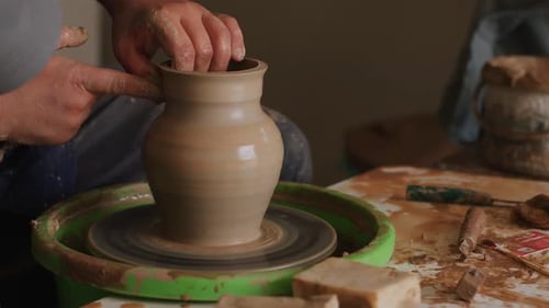Un artisan fabrique une cruche en argile sur un tour de potier dans un atelier, gros plan de mains masculines créant des objets uniques