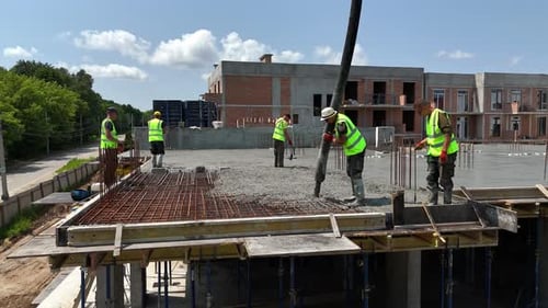 Bauarbeiter in Sicherheitswesten gießen Beton auf die oberste Stockwerkplatte der Baustelle — Teamwork