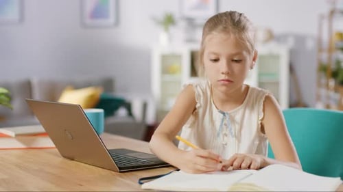 Smart Little Girl Does Homework in Her Living Room. She's Sitting at Her Desk, Uses Laptop and Writ