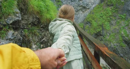 Girl walking along the duckboards in rocky gorge. A woman holds a man's hand and calls him to follow