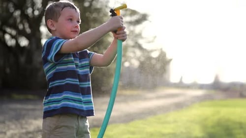 Young boy spraying water hose in backyard on sunny summer day
