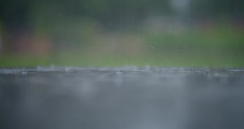 Rain Falling on Wet Glass with Blurred Green Background and Reflective Water Below