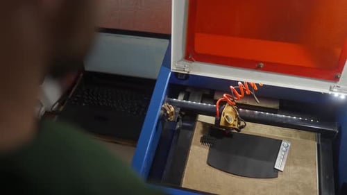 Over Shoulder View of Leather Craftsman Controlling Laser Engraving Machine in Process of Applying