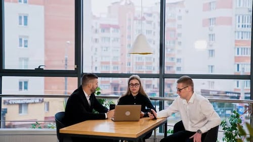Serious confident young team sitting in the office in front of laptop and talking.