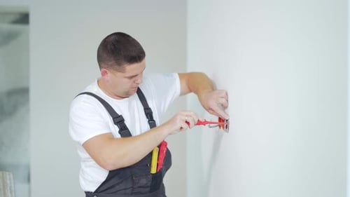 Male worker professional qualified electrician installs electrical outlet in apartment after repair.