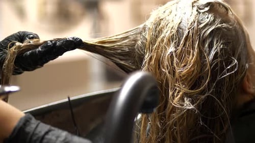 Close-up slomo from behind of blonde female hair being dyed at salon