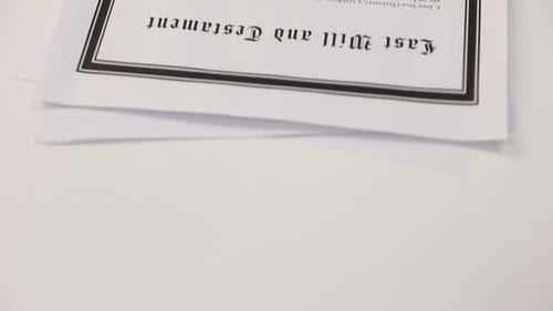 Mulher assinando o Último Testamento e o Testamento na mesa branca, em closeup. Câmera se movendo para cima