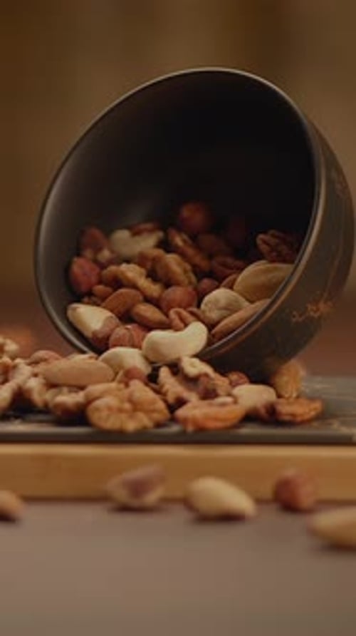 A Colorful Mixture of Assorted Nuts is Spilling Out From a Bowl on a Wooden Surface