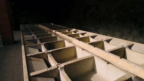 Structure en treillis de béton, probablement d'anciens réservoirs ou cuves industriels, partiellement éclairée dans une pièce en pierre,...