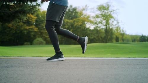 Close Up Athlete In Sports Shoes Jogging On Road. Man Legs Training Outdoors In Slow Motion. Male...
