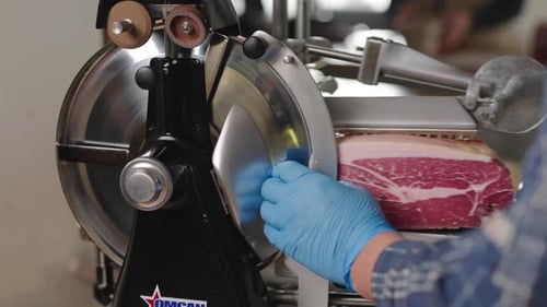 Prosciutto being sliced by hand at an Italian deli. Fresh deli meat being sliced on a meat slicer.