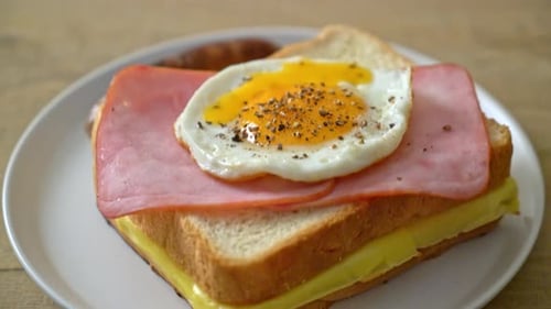 homemade bread toasted cheese topped ham and fried egg with pork sausage for breakfast