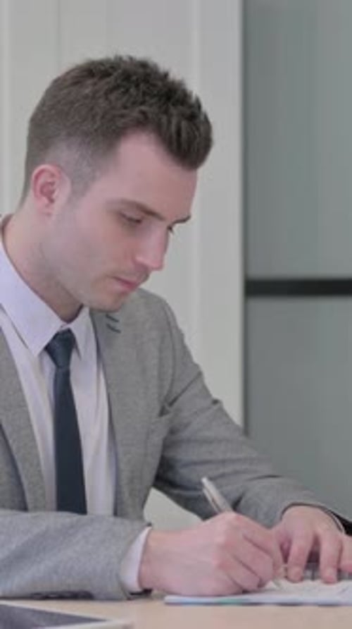 Young Adult Man Writes on Document in Workplace