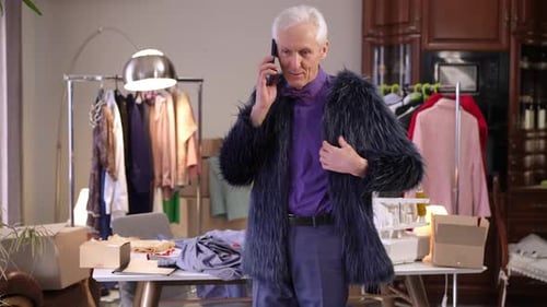 Ein stilvoller extravaganter älterer männlicher Modedesigner spricht mit einem Handy, während er darin steht