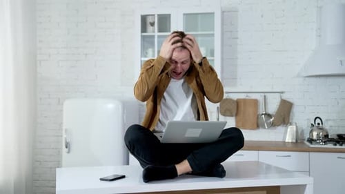 Man Reacts to Bad News on Laptop in Kitchen