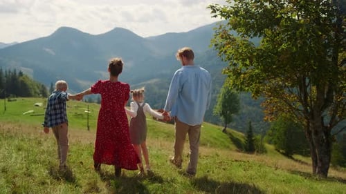 Family enjoying summer vacation walking on mountains hill sunny day back view